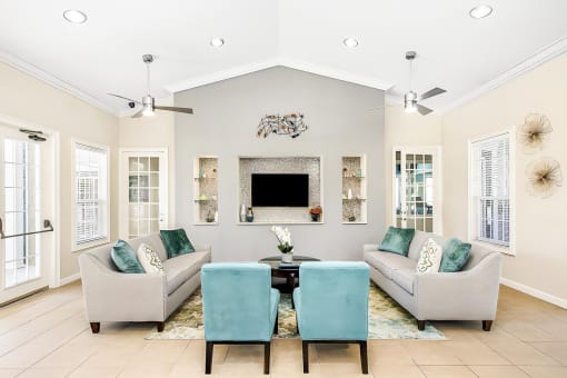 Interior of the clubhouse with tile flooring, couches, coffee table, rug, mounted tv and 2 ceiling fans