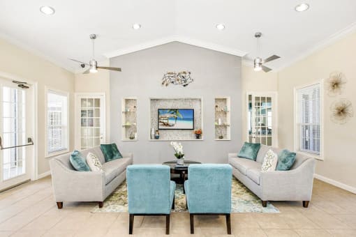 Interior of the clubhouse with tile flooring, couches, coffee table, rug, mounted tv and 2 ceiling fans