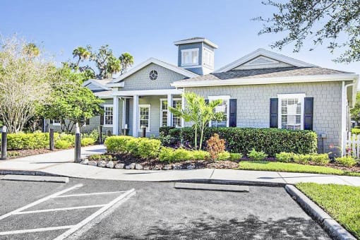 Clubhouse Entrance surrounded by shrubbery and trees with view of parking lot