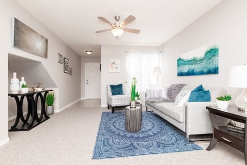 Furnished living room with couch, accent chair, area rug, and ceiling fan.