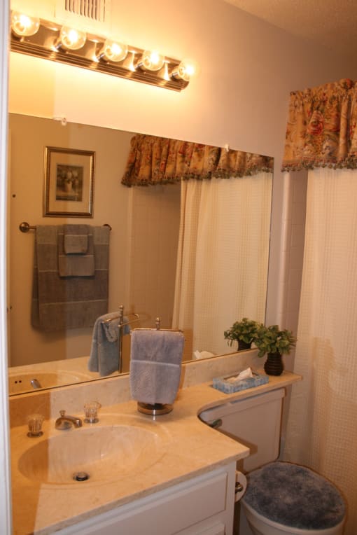 Staged bathroom with granite style countertops, white cabinets, large vanity mirror, shower and tub with white tile walls, white shower curtain, and gray towels.