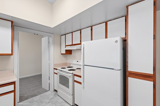 A white refrigerator is in a kitchen with a white oven and wooden cabinets.