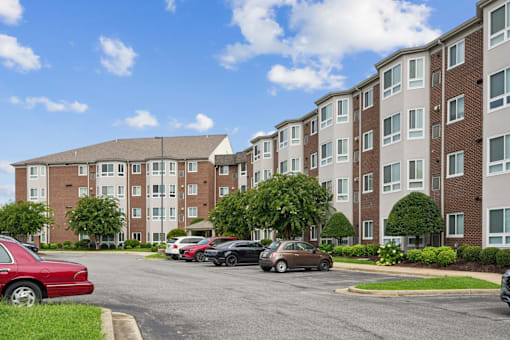 A red car is parked in a parking lot in front of a brick apartment building.