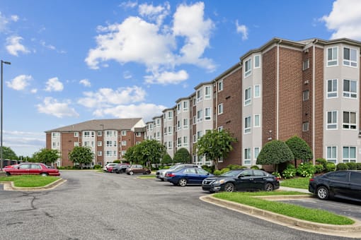 A parking lot in front of apartment buildings with cars parked.