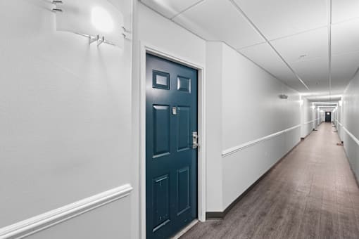 A long hallway with a blue door and white walls.