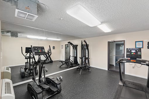 A gym with treadmilers, elliptical machines, and a weight rack.