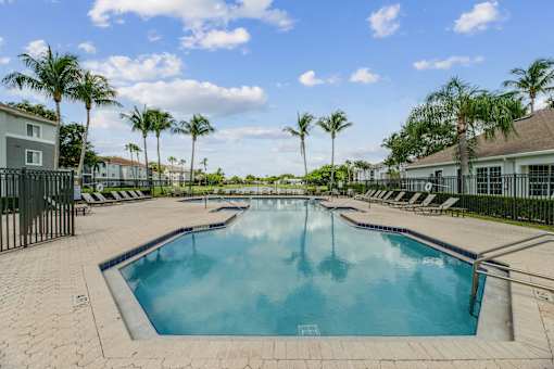 A large outdoor swimming pool surrounded by palm trees and lounge chairs.