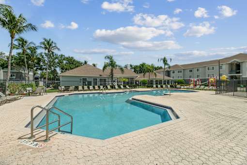 A large swimming pool surrounded by a brick patio and palm trees.