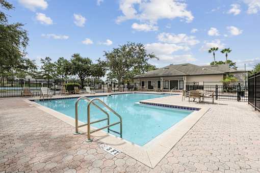 A pool surrounded by a brick patio and a metal fence.