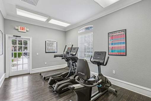 A gym with treadmills and a red exit sign.