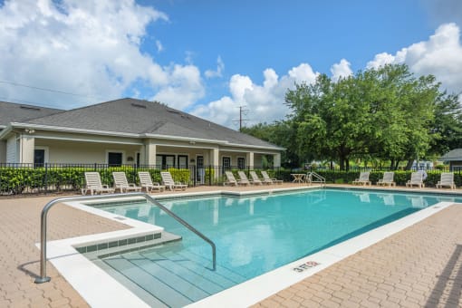 Swimming pool surrounded by lounge chairs with clubhouse in the background