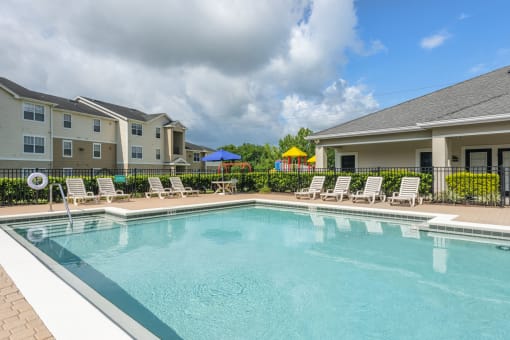 Swimming pool with lounge chairs. view of an apartment building, playground and clubhouse in the background