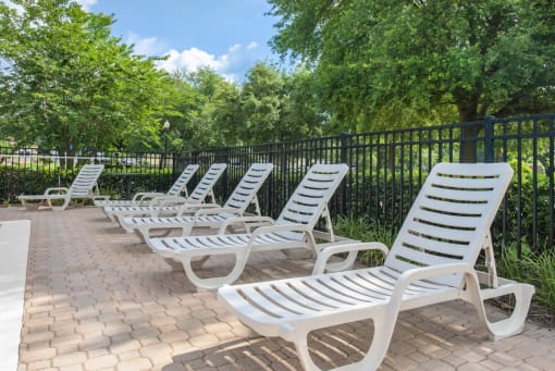a row of chaise lounges on a brick patio with trees in the background