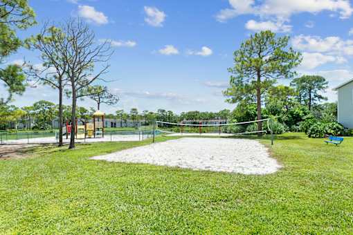 A volleyball court on sand, surrounded by a fence and trees.