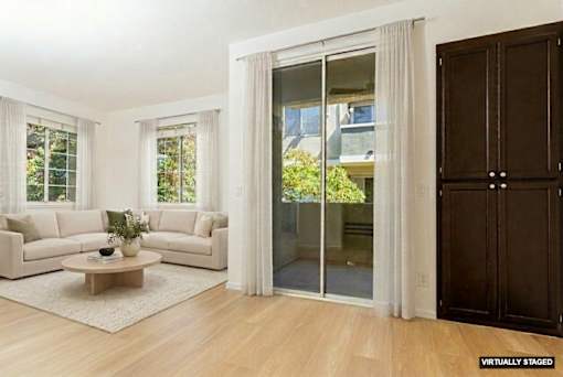A living room with a white couch, a coffee table, and a glass door leading to a balcony.