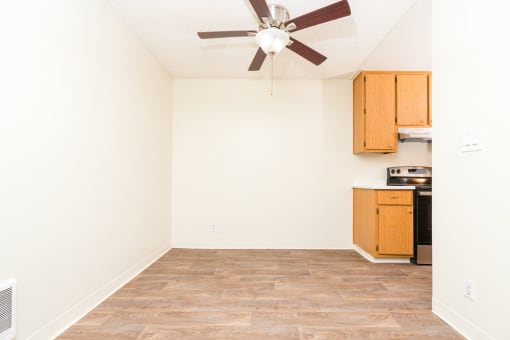 an empty room with a ceiling fan and a kitchen