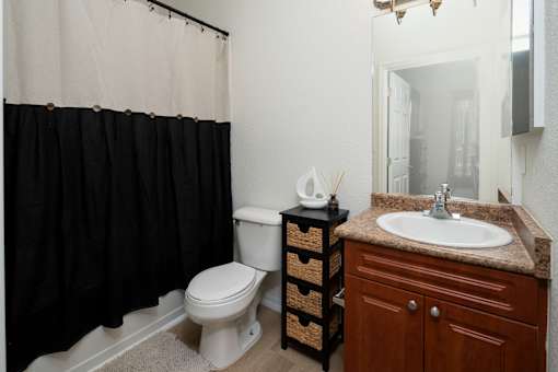 A bathroom with a white toilet, a brown cabinet, and a black shower curtain.