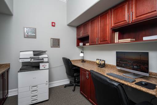 A white printer sits on a desk next to a black chair.