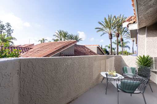 A patio with a table set for two and a view of a roof and palm trees.