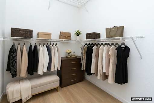 A white closet with clothes hanging and a bench underneath.