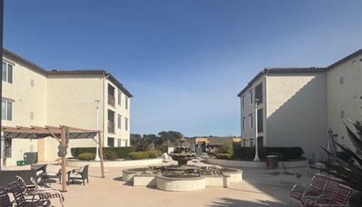 A courtyard with a fountain and chairs is surrounded by buildings.