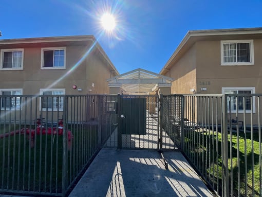 an apartment building with a fence and gate with the sun shining over it