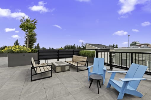 Two Blue Adirondack Chairs with two wooden benches facing cozy fireplace on the Resident Rooftop Lounge with a blue sky in the background at Arabella Apartment Homes, Shoreline, Washington 98155