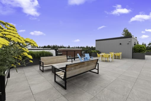 a roof terrace with a benches facing the cozy firepit with chairs and yellow flowers at Arabella Apartment Homes, WA 98155