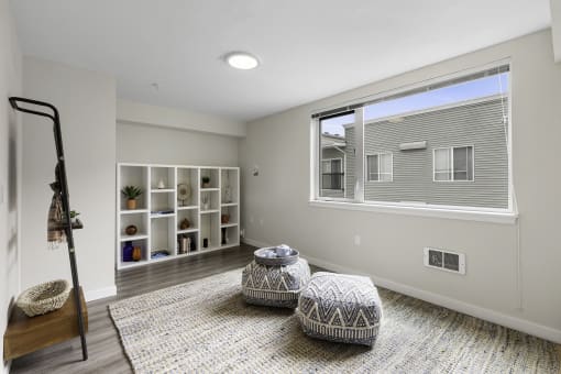 Cozy Living Area with Plank Flooring, Spacious Cozy Rugs, White Bookshelving, a large window and two stools in the middle of the room at Arabella Apartment Homes, Washington, 98155