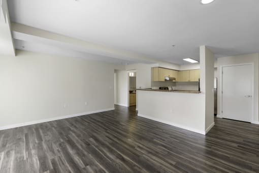Unfurnished living room with plank flooring, tall ceilings, and a kitchen in the background at Arabella Apartment Homes, Washington, 98155
