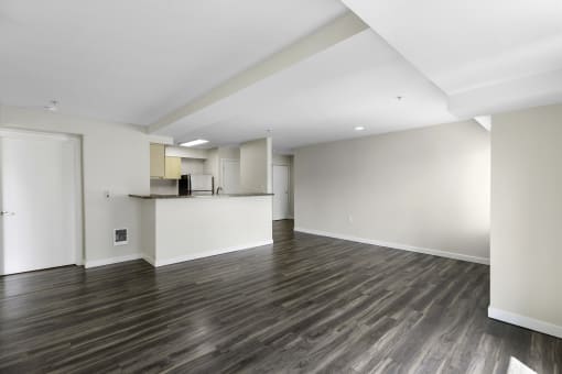 An Unfurnished living room with dark plank flooring, recessed lighting, and tons of space with a view of the kitchen in the background at Arabella Apartment Homes, WA 98155
