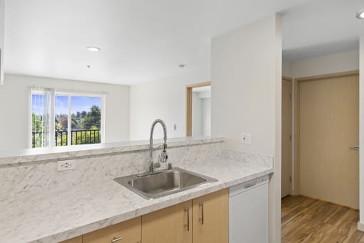 a kitchen with a sink and under sink cabinets with a view of the living space complete with sliding glass doors at Guinevere Apartment Homes, Seattle, Washington 98103
