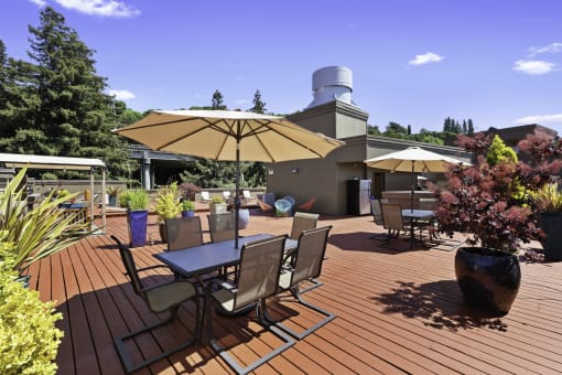 a large wooden deck with tables and chairs for lounging and potted flowers at Illumina Apartment Homes, Washington, 98102