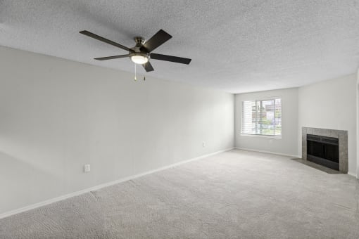 an open living room with a fireplace and a ceiling fan at Willows Court Apartment Homes, WA 98125