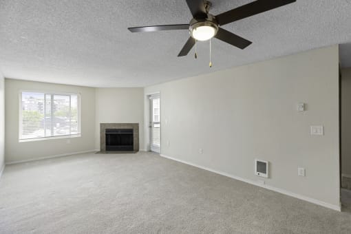 a living room with a fireplace, cozy carpeting, oversized windows, and a ceiling fan at Willows Court Apartment Homes, Seattle, WA