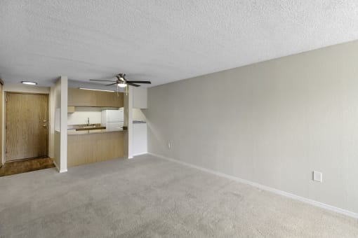 an unfurnished living room with a ceiling fan and a kitchen in the background at Willows Court Apartment Homes, Seattle, 98125
