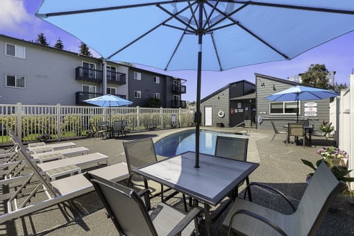 a patio with a pool and chairs and umbrellas at Pacific Park Apartment Homes, WA 98026
