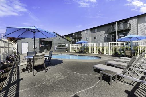 a patio with a pool and chairs and umbrellas at Pacific Park Apartment Homes, Washington