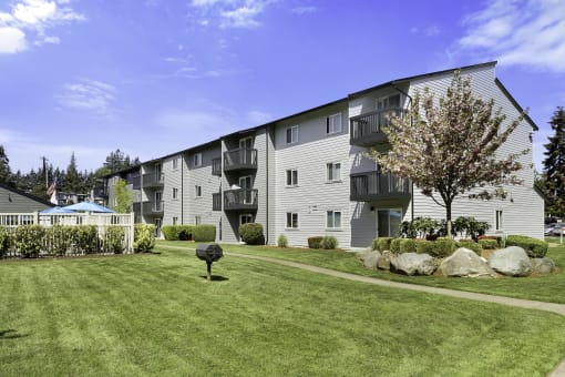 a grassy area with a tree in front of an apartment building at Pacific Park Apartment Homes, Edmonds, WA