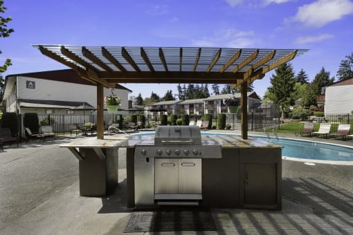 Decadent Resident Outdoor Kitchen with a Shaded Wooden Pergola Next to the Sparkling Swimming Pool at Pinewood Square Apartment Homes, Lynnwood, WA