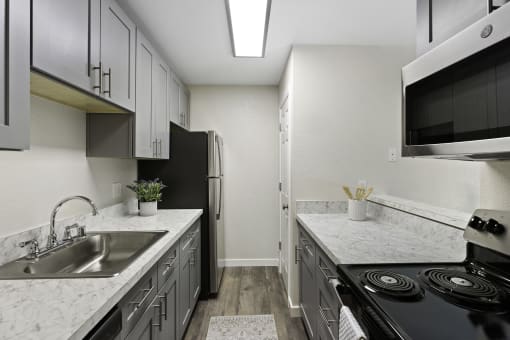 Kitchen With Chic Finishes like Stainless Steel Appliances, Plank Flooring, and Elegant Cabinetry at Pinewood Square Apartment Homes, Lynnwood, 98087