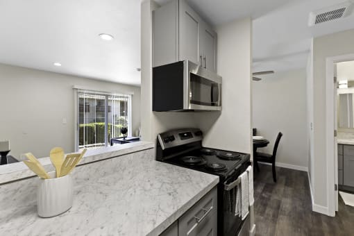 Cozhy Kitchen with Stainless Steel Appliances, Plank Flooring, Spacious Cabinetry, and View of the Living Area at Pinewood Square Apartment Homes, Lynnwood, WA