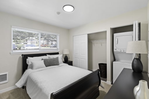 a bedroom with a bed and a dresser with a washer and dryer at Pinewood Square Apartment Homes, Lynnwood, Washington 98087