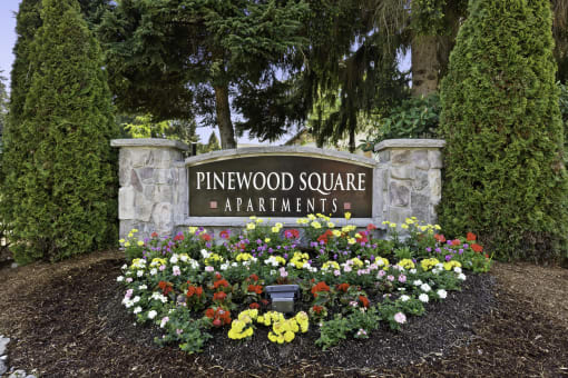 Stone Welcome Sign to Pinewood Square Apartment Homes with Flower Bed Below at Pinewood Square Apartment Homes, WA 98087