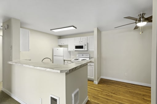 a kitchen with an island, plank flooring, overhead lighting, and a ceiling fan in the dining area at Serra Vista Apartment Homes, Lynnwood, Washington 98087