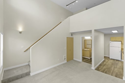 Loft-Style Apartment with Sconce Lighting Up Stairs to Living Area, Plush Carpeting, and Kitchen View in the Background at Sir Gallahad Apartment Homes, Bellevue