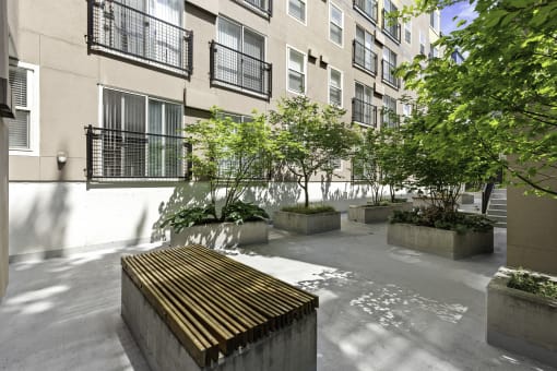 a courtyard with a wooden bench and trees in front of  Sir Gallahad Apartment Homes, Washington, 98004