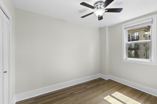 a bedroom with hardwood floors, a large window, and a ceiling fan with light at Stockbridge Apartment Homes, Seattle