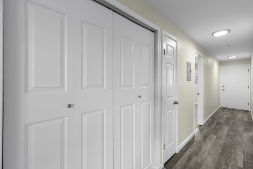 a long hallway with white closet doors and white walls at Swiss Gables Apartment Homes, Kent, WA