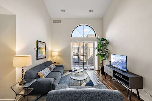 A living room with a grey couch, a television, and a large window at MainCentre, Northville